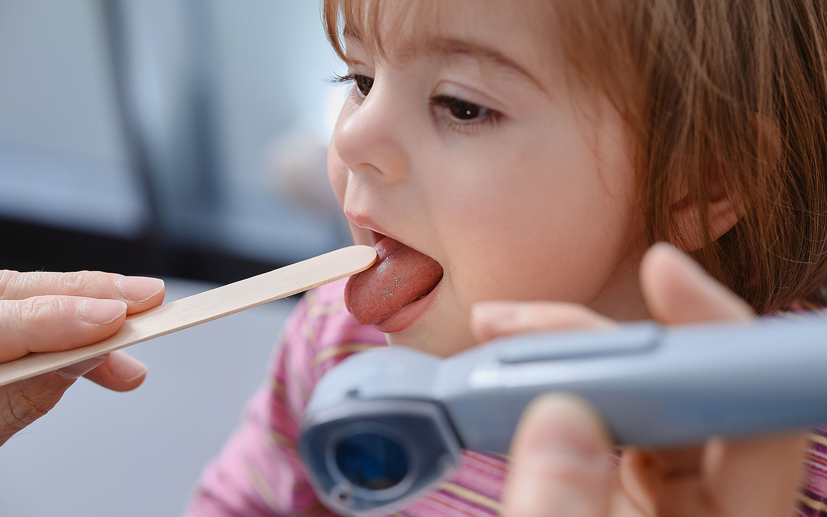Medizinische Untersuchung von Zunge und Rachen eines Kindes mit Holzstab - Informationen zu Attesten für KiTa und Schule