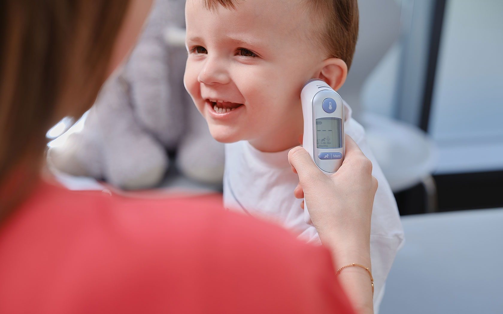 Lächelndes Kind bekommt Fieber am Ohr gemessen – Zur Themenseite Häufige Krankheiten